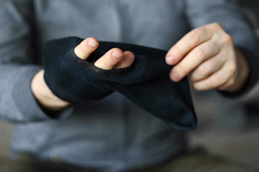 Man pass fingers thru big hole in black sock close-up