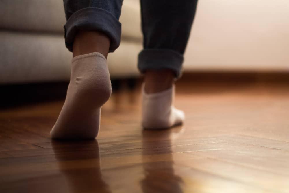 Legs of a woman in jeans and socks walking on the wooden floor