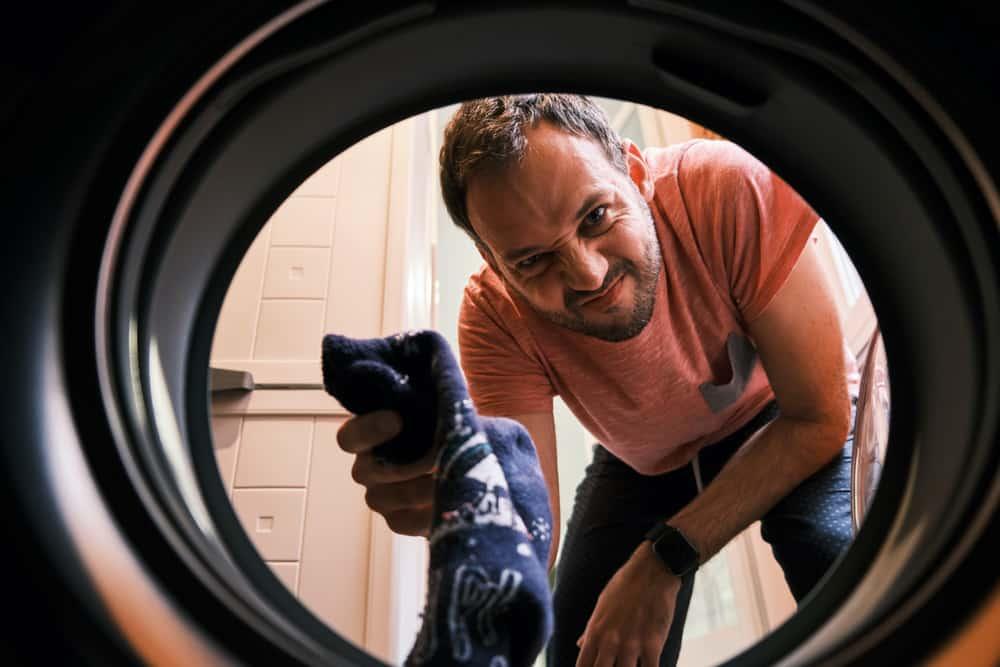 A Man Puts A Pair Of Dirty Socks Inside The Laundry Machine For Washing