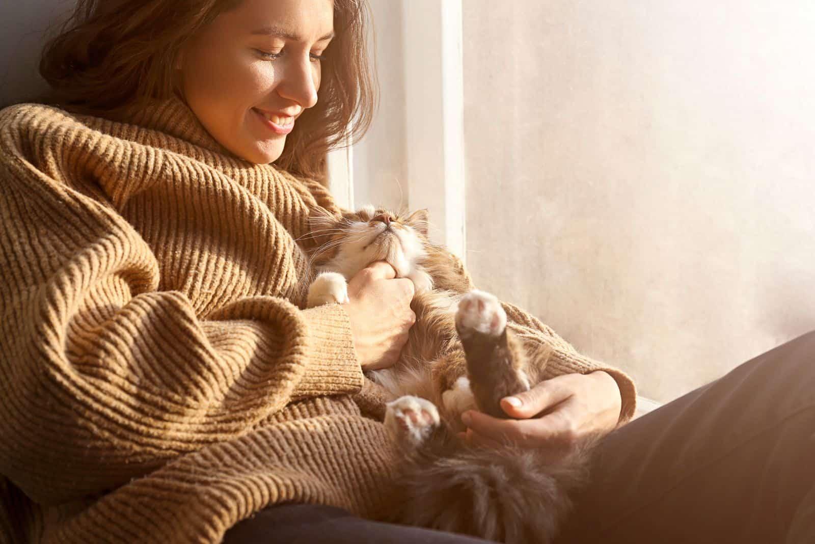 young woman holding cute Siberian cat with green eyes in her arms