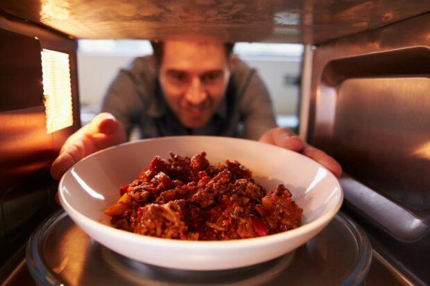 Man reaching into microwave for bowl of food after learning why the microwave spins