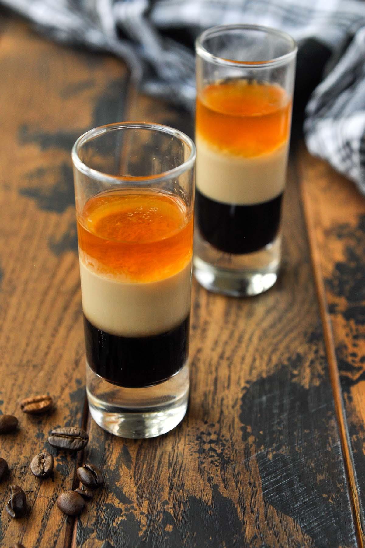 Up close of two shots of the duck fart shot with a bottle of Irish cream in the background.