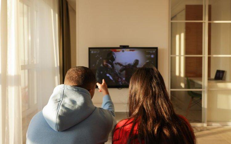 two people watching a dim TV in a bright room