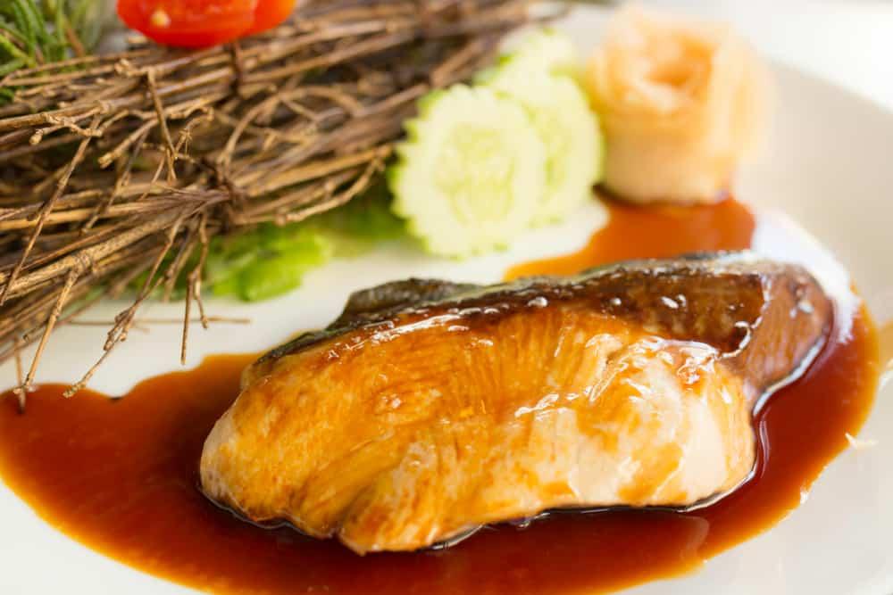 close up of grilled sablefish with soy sauce on white plate