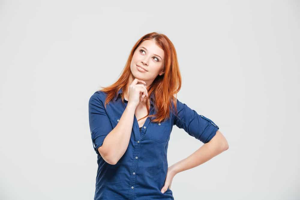Pensive happy cute redhead young woman thinking over white background