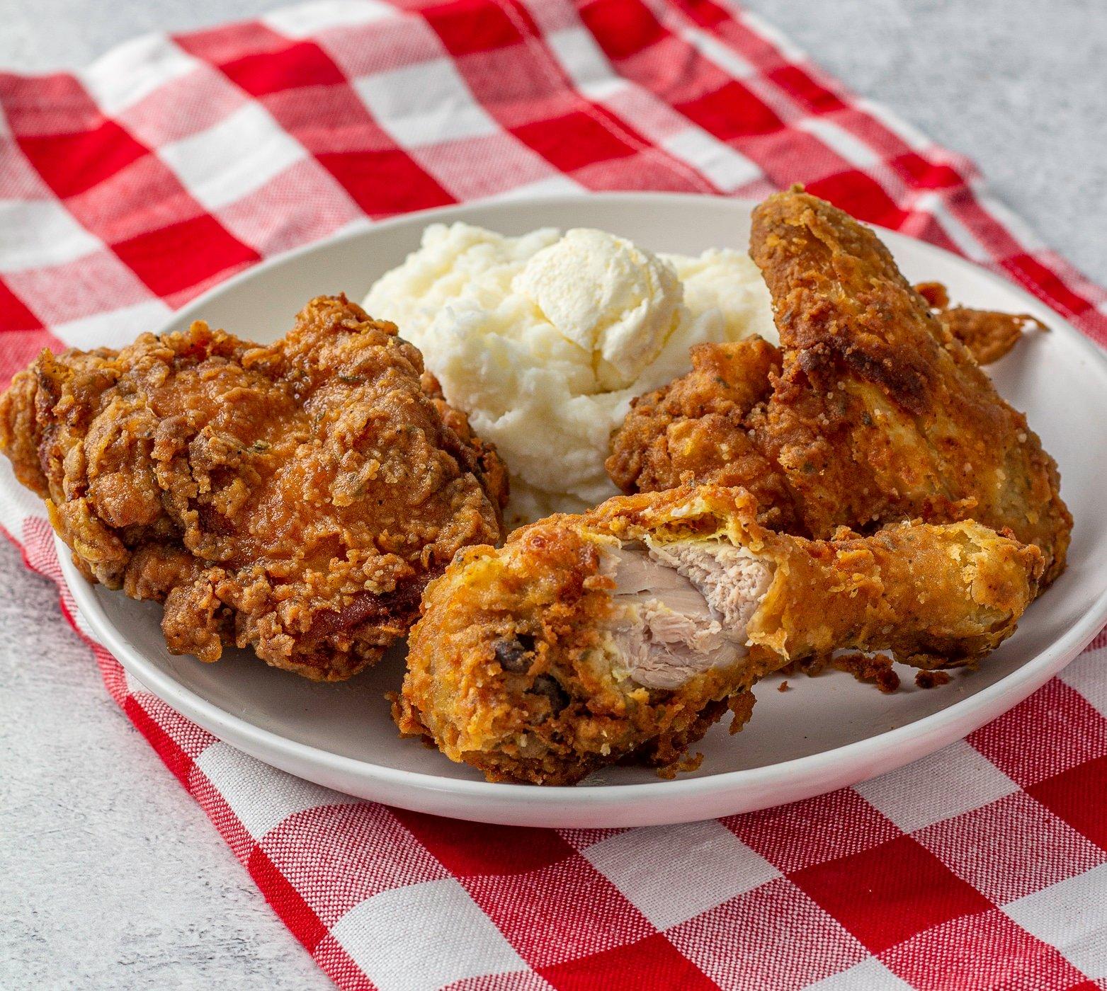 Deep fried chicken and mashed potatoes on a white plate, sitting atop a red checked napkin.