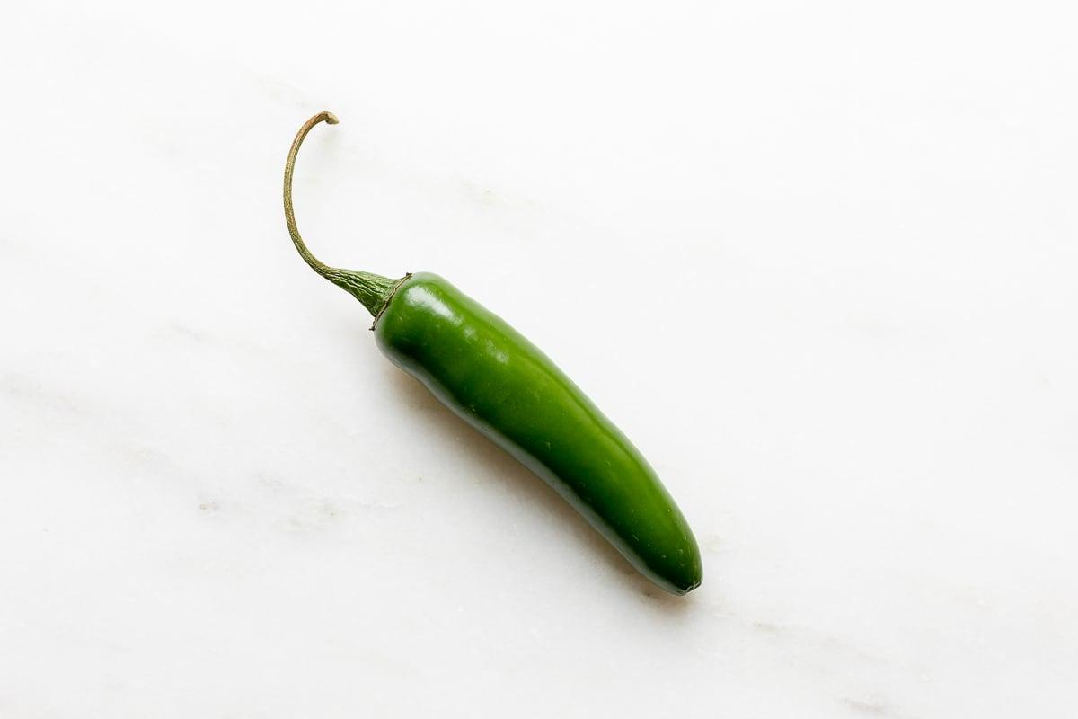 A jalapeno pepper on a white marble countertop.