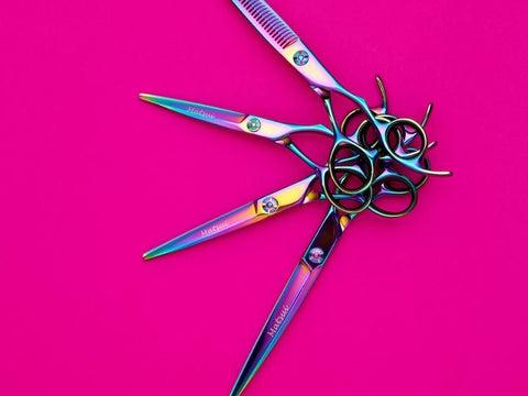 Professional hairdressing scissors placed in a semi-circular array on bright pink background.