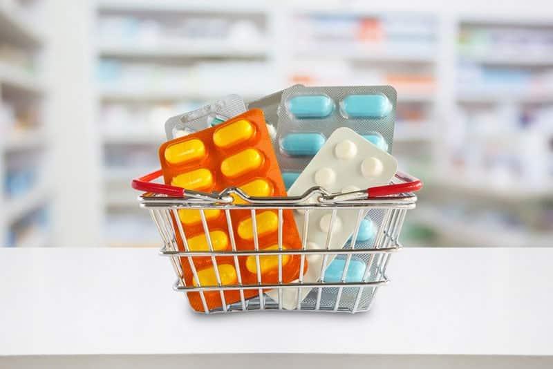 medicine pills package in shopping basket with pharmacy blurred background