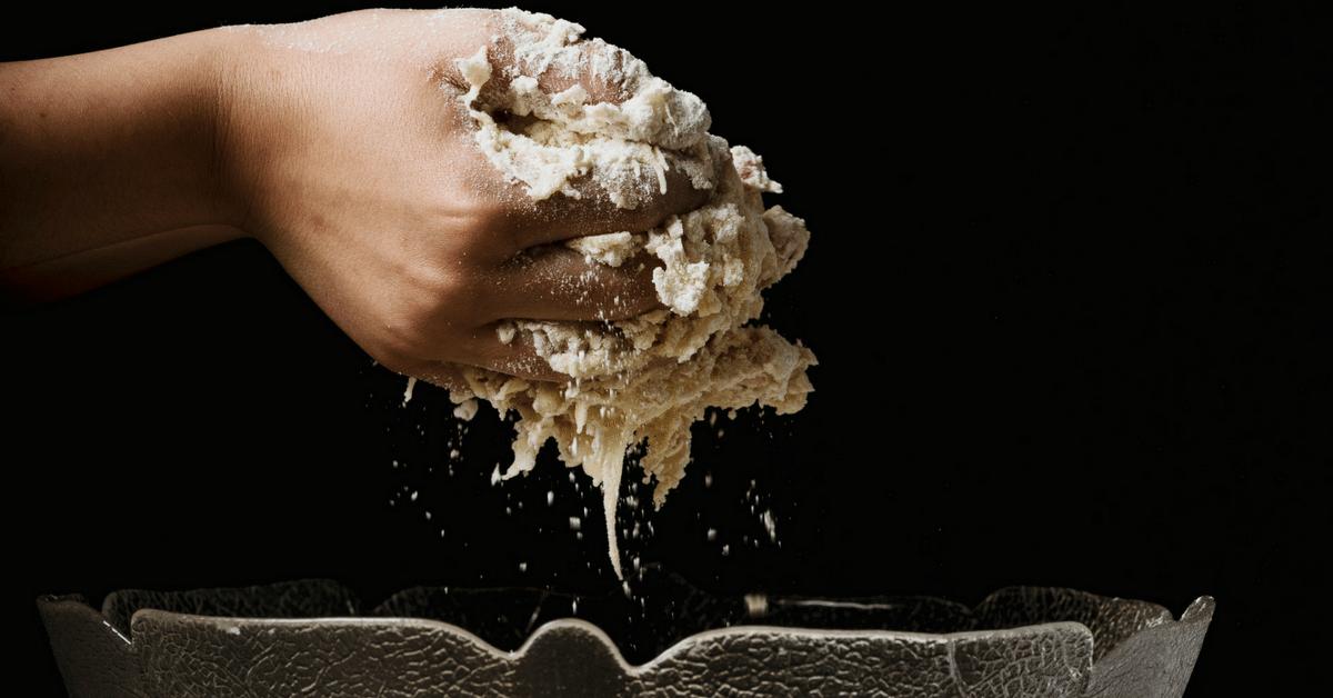 Hands lifting dough out of a clear bowl.