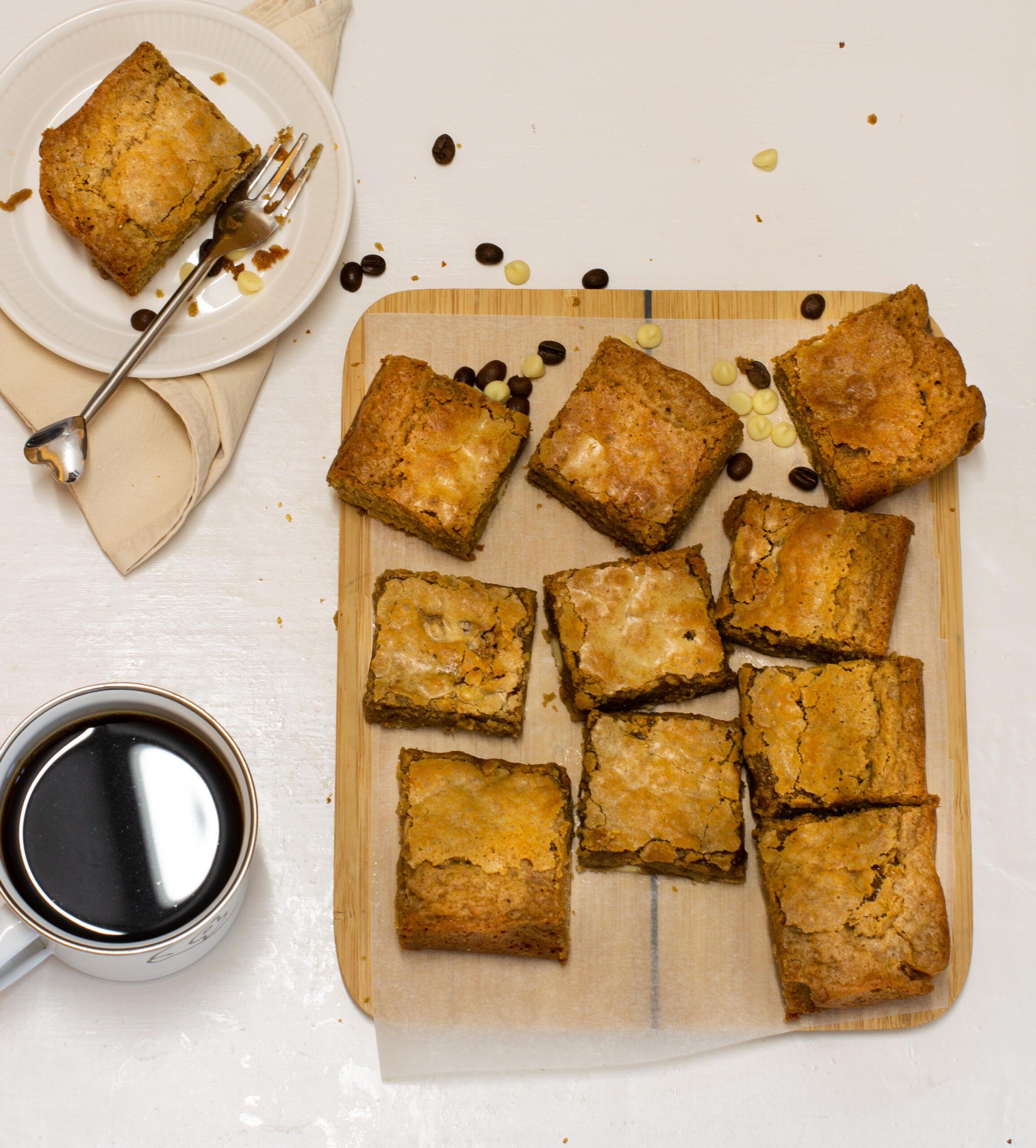 Two white chocolate blondies on a plate with cake forks and blue tea towel