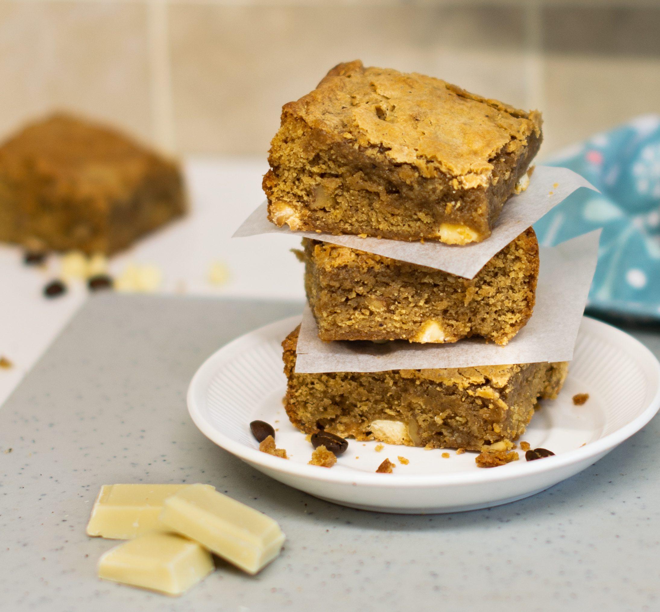 Stack of three blondies on a plate beside blue tea towel and white chocolate