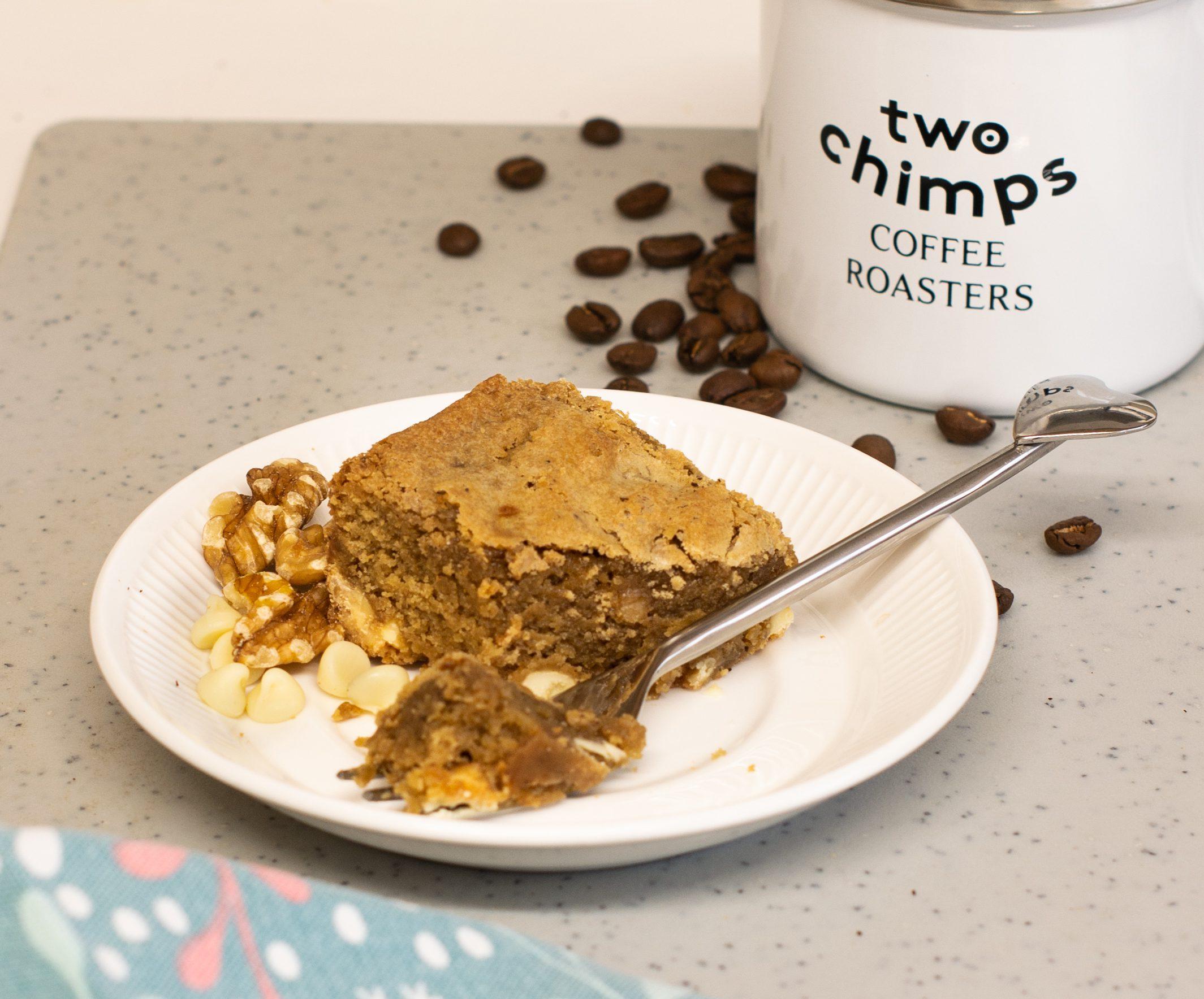 Coffee and walnut blondie on a plate with a cake fork and mug of Two Chimps specialty coffee