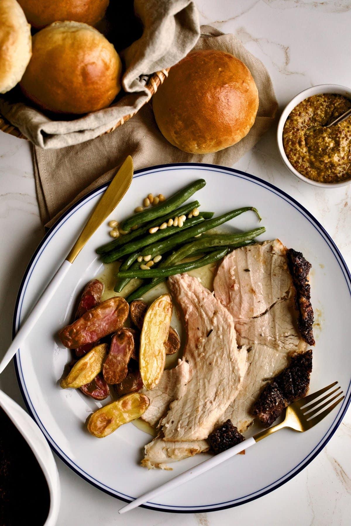 fresh ham roast on a plate with roasted potatoes and green beans.