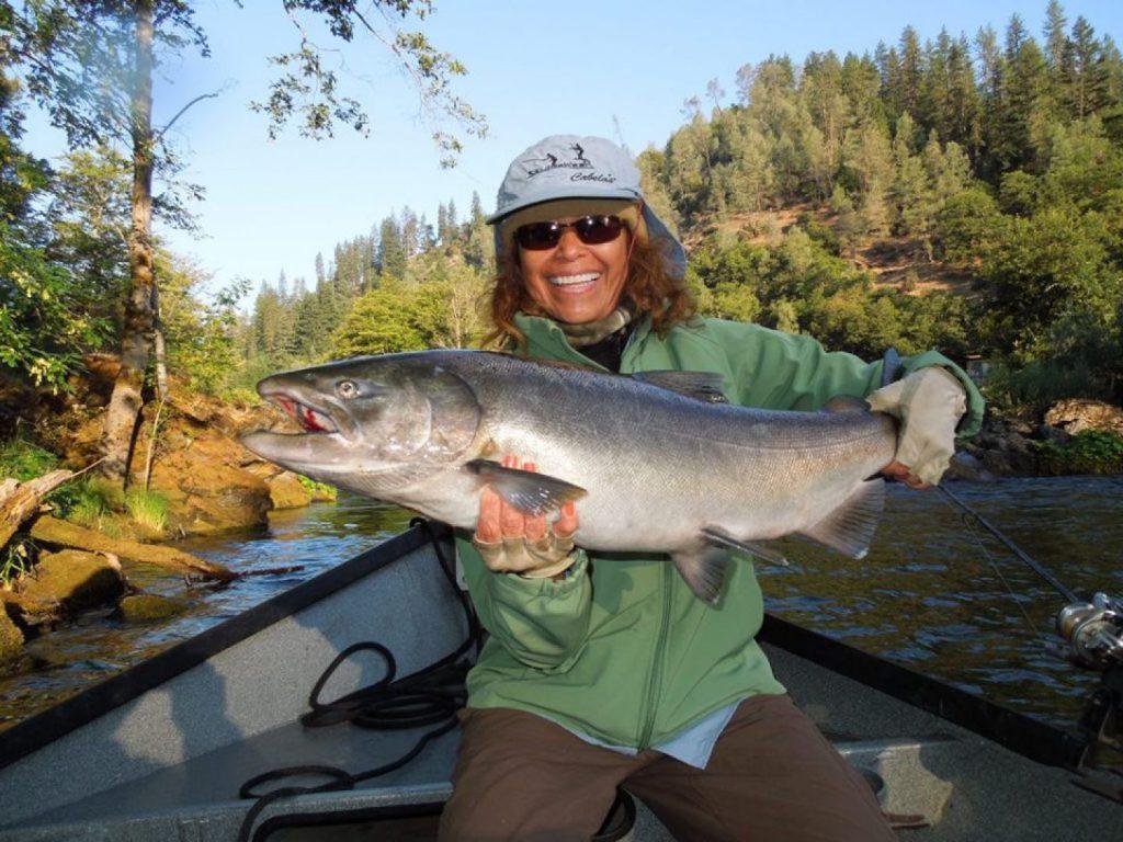 a smiling female angler holding a salmon on a fishing boat