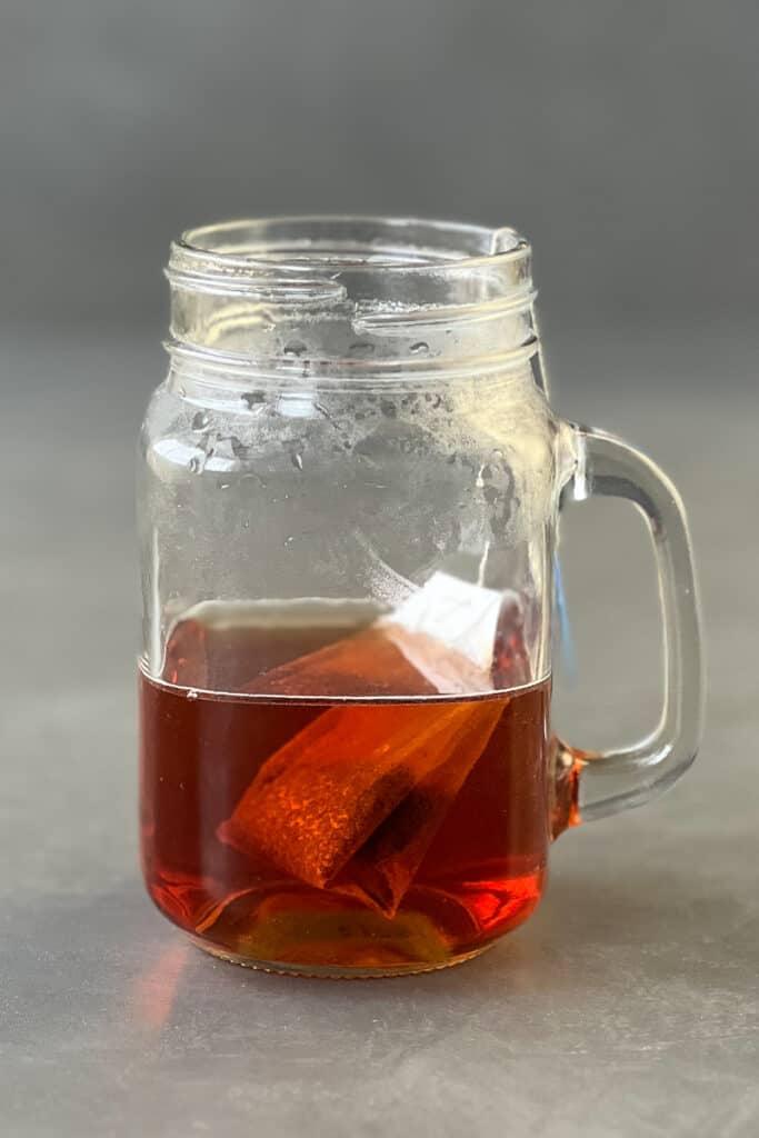 Half filled mason jar with tea and tea bag in it.