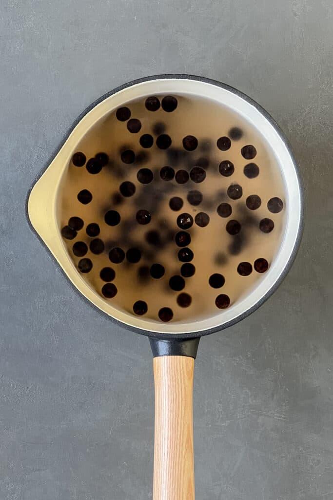 A saucepan with a water and cooked tapioca boba pearls in it.