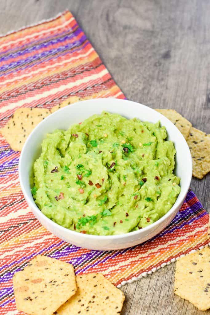 hand holding up a chip with guacamole dip on it over the bowl.