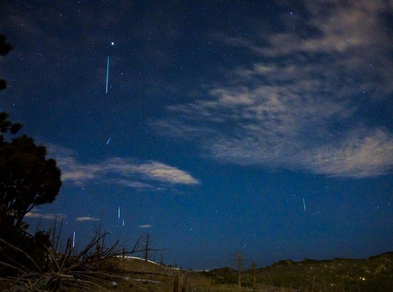 Dark blue sky with a few clouds and stars and vertical white streaks.