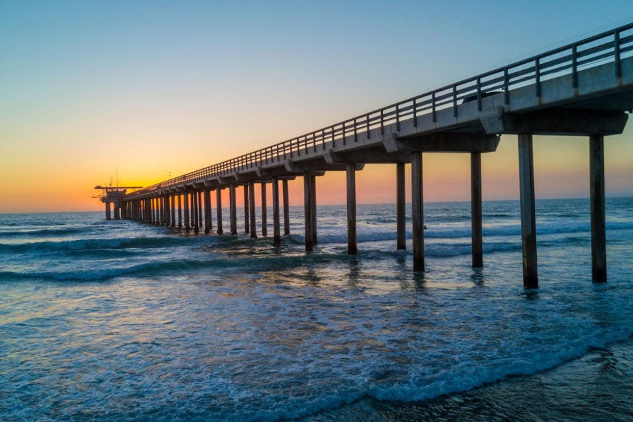 Scripps Pier in San Diego. The sun is setting behind the pier and there is nobody in the calm waters of La Jolla.