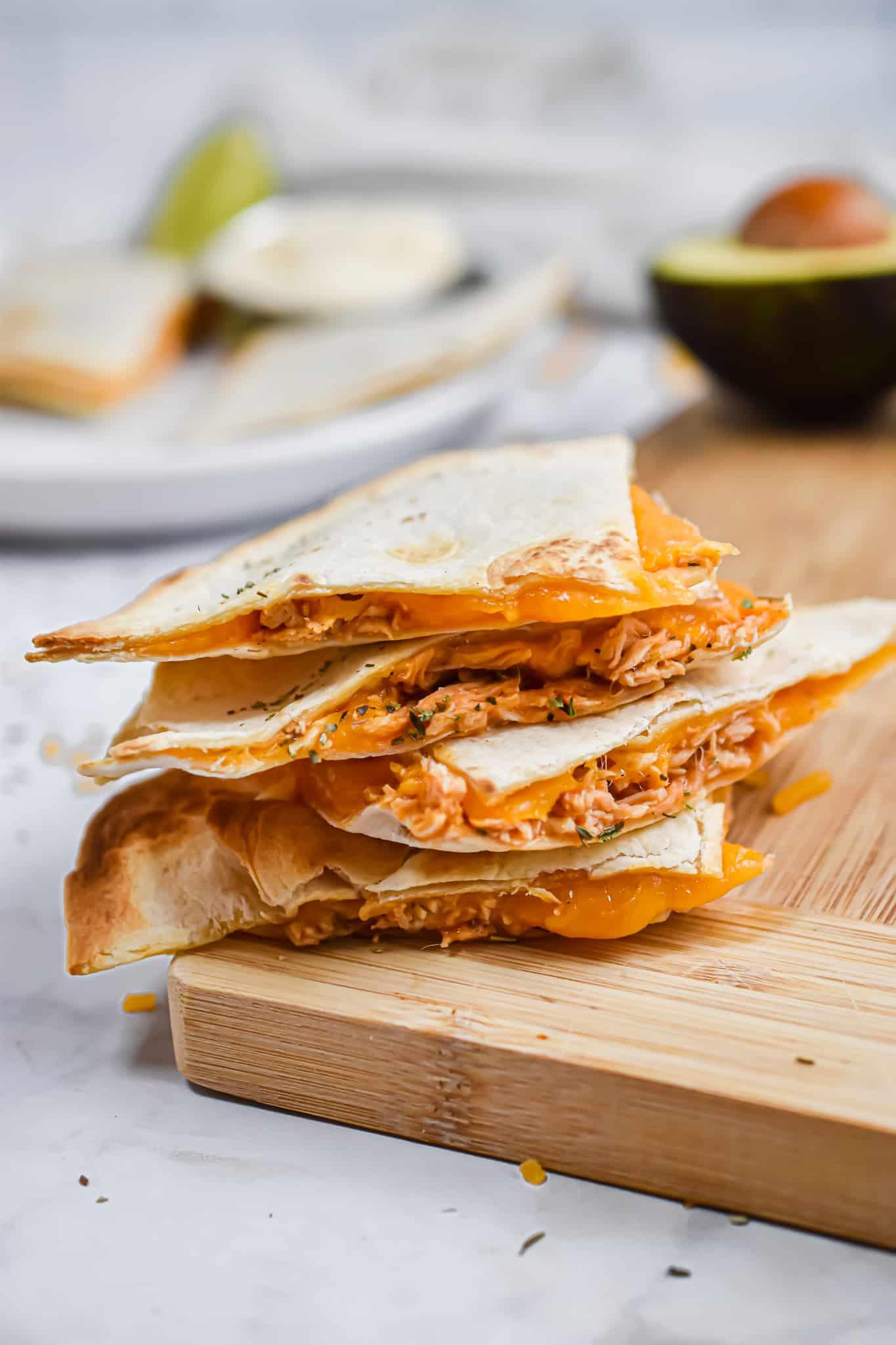 The buffalo chicken sheet pan quesadillas are stacked on top of a wooden cutting board.