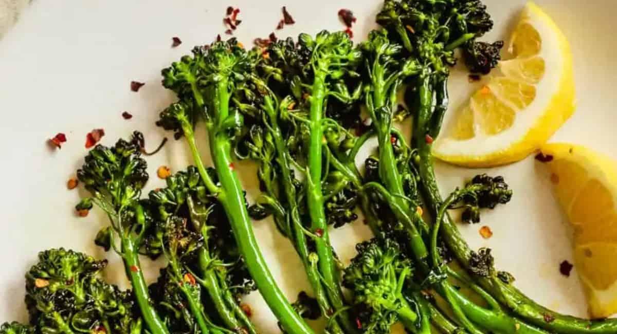 Broccolini served on a white plate as a side for meatball subs.