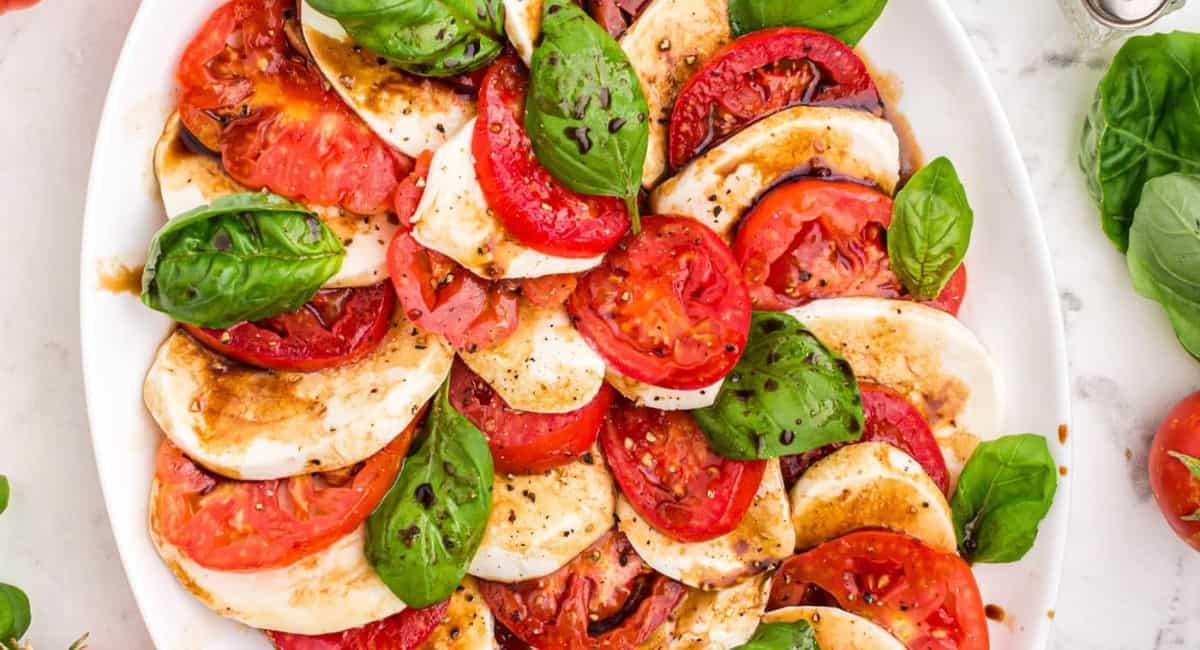 Caprese salad with tomato, mozzarella and basil on a white plate.