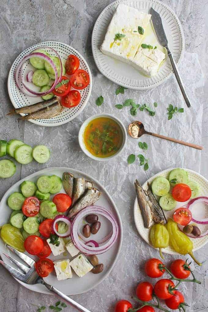 Plates of Greek salad with sardines on them with a plate of feta cheese.