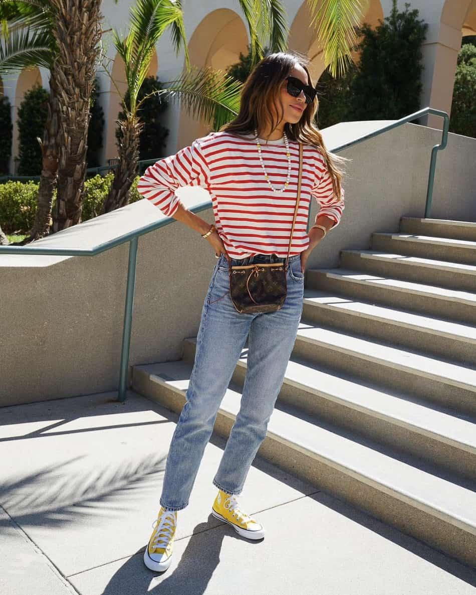 A woman wearing blue jeans, a white and red striped long-sleeved tee, and yellow converse sneakers