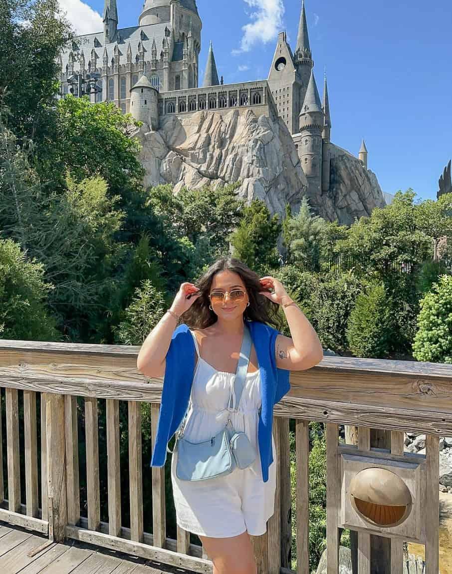 A woman at Universal Studios wearing a white romper with a bright blue sweater draped over her shoulders and a pastel blue purse