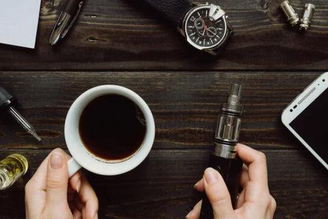 a person holding a cup of coffee and a vape