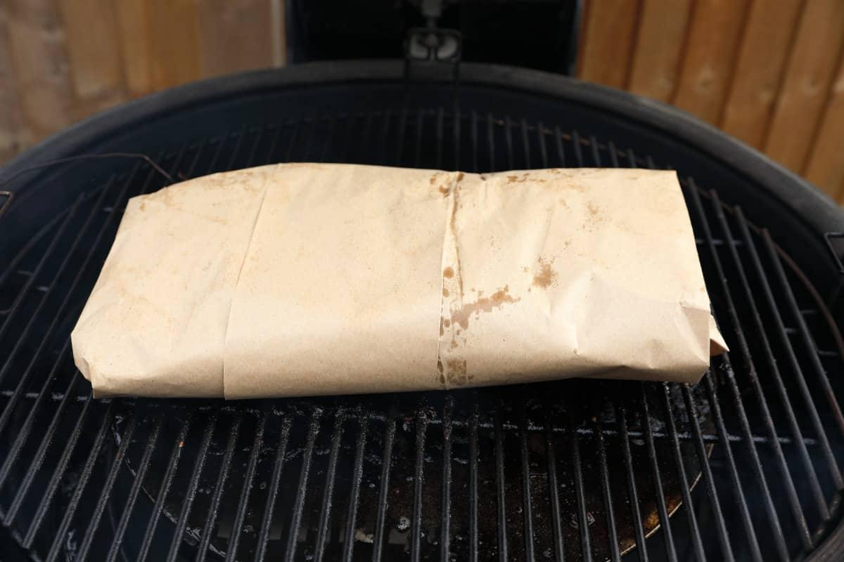 A pink butcher paper wrapped brisket on a kamado style smo.