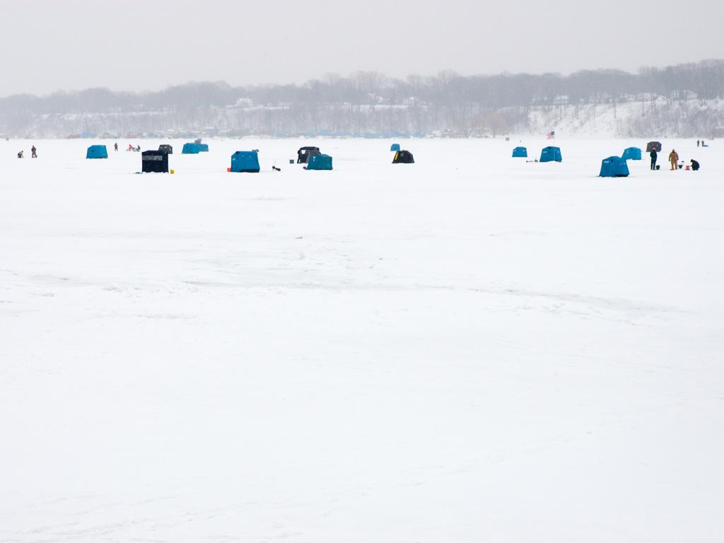 Multiple ice fishing shanties set up on Lake Erie, along with anglers walking on ice.
