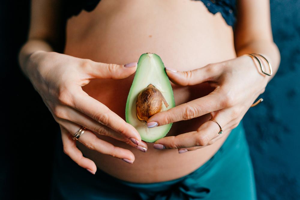 pregnant woman holding an avocado to her belly to show size of fetus