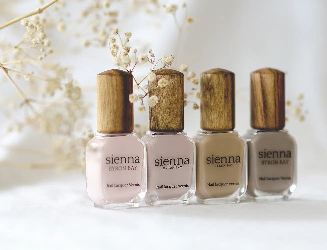 4 neutral nail polish bottles with timber cap by sienna with baby breath in the background
