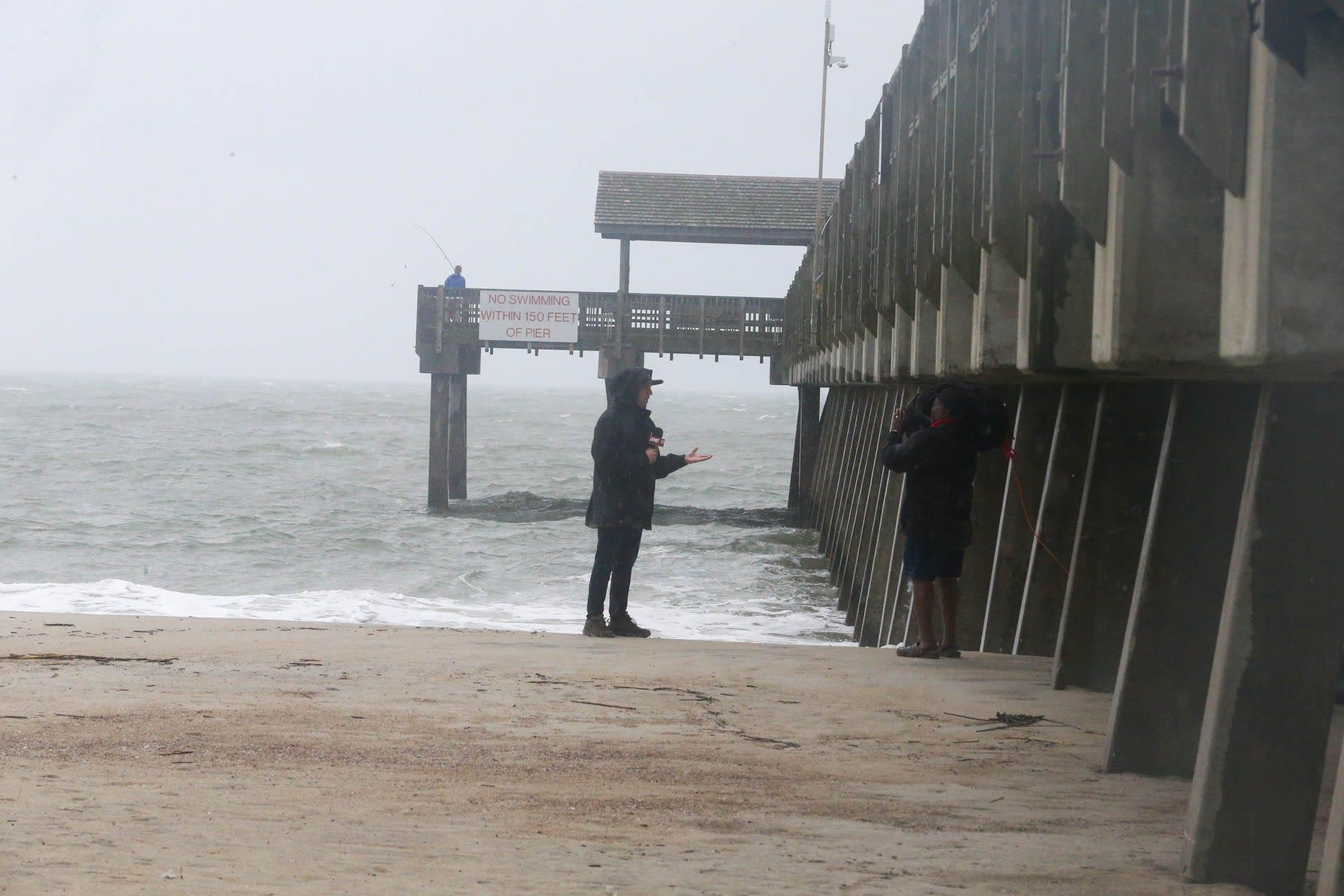 A lone fisherman fishes from the Tybee Island Pier as a news crew reports from Tybee Island, Georgia on Wednesday, August 30, 2023 as Hurricane Idalia made landfall in Florida.