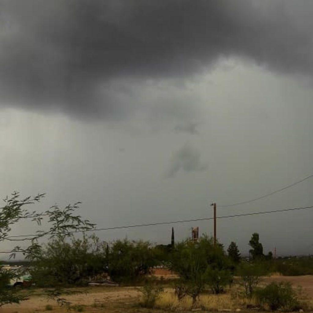 Rain beginning to fall from dark clouds over a rural area.