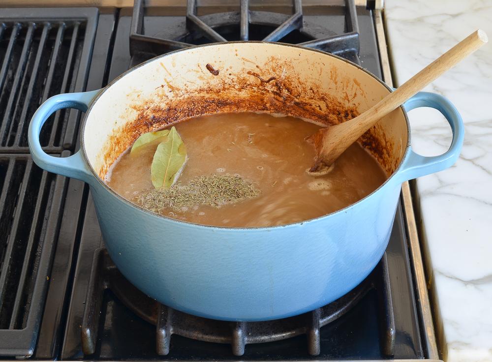 adding broth and herbs to pot