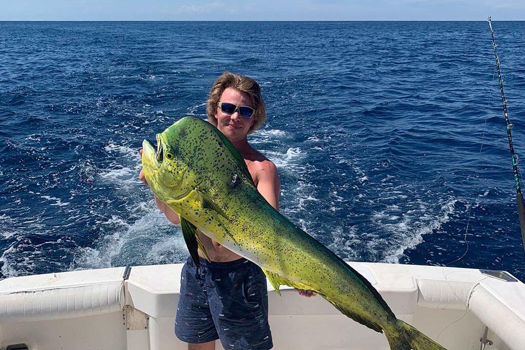 An angler stands while holding a Mahi Mahi freshly caught in the Gulf.