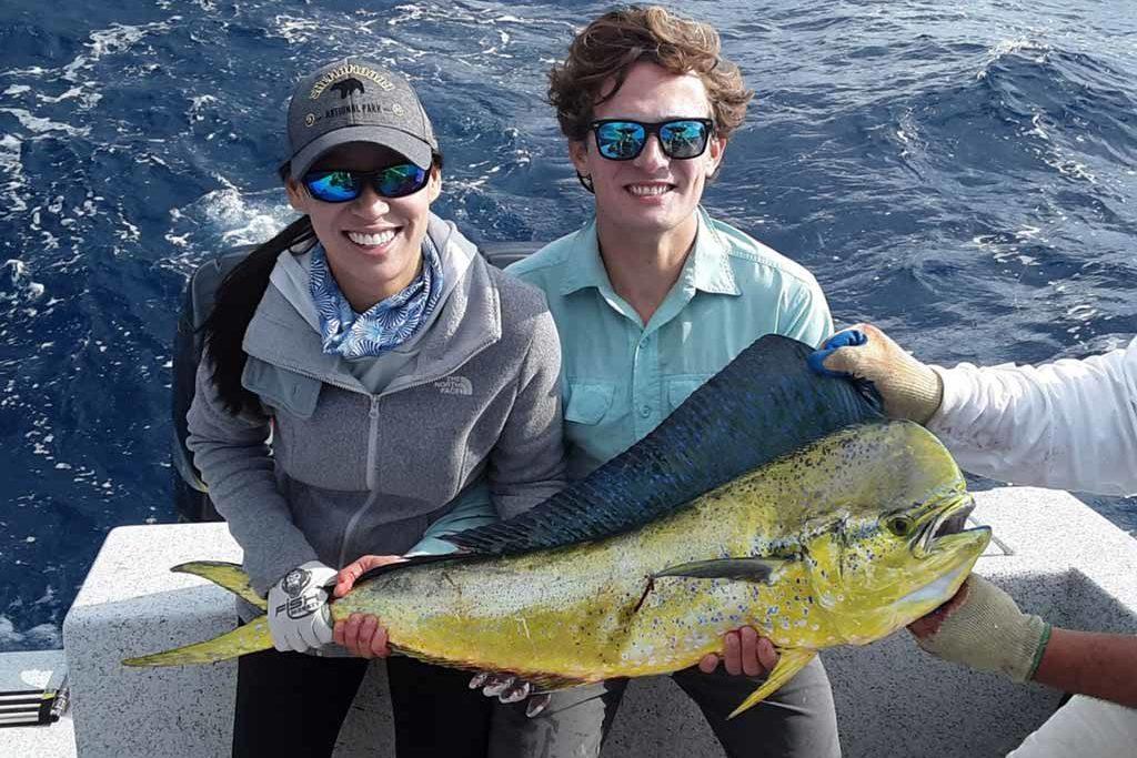 A couple on a boat, smiling and holding a Mahi Mahi.