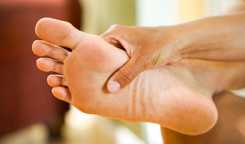 A person pressing their thumb into the sole of their foot, just behind the ball of their foot