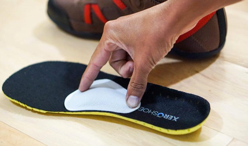 A hand temporarily placing a Pedag metatarsal pad in the middle of a shoe insole