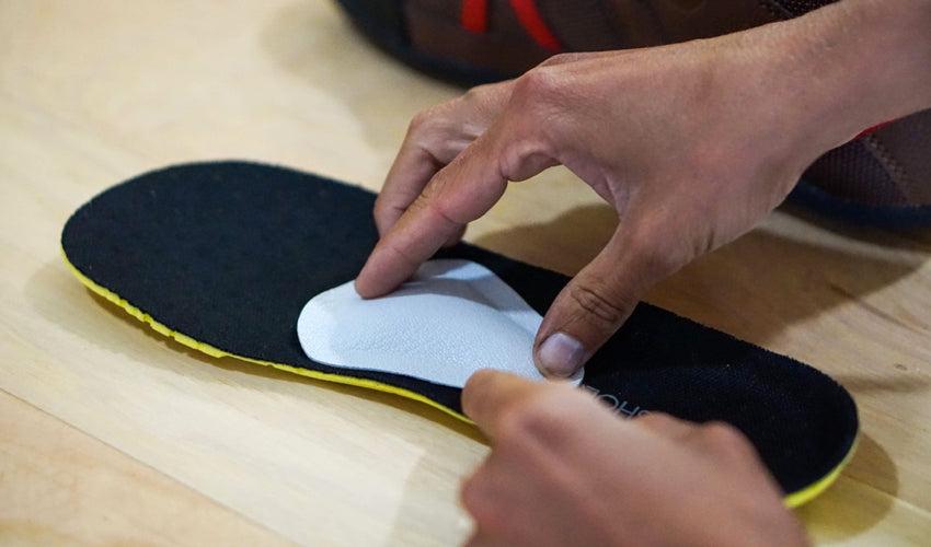 A set of hands making positional adjustments to a Pedag metatarsal pad situated on top of a shoe insole