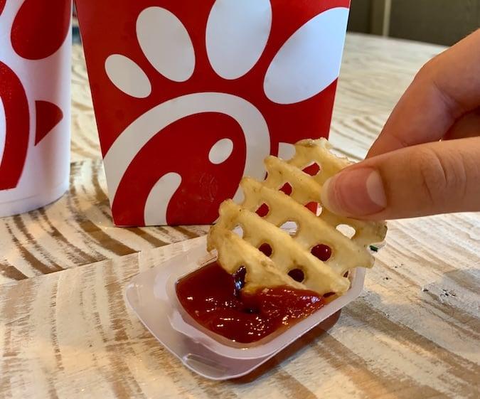 hand dipping gluten-free chick-fil-a waffle fry in ketchup