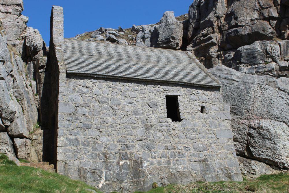 The chapel is grey and clearly very small: stone walls, simple slate roof, and it is built up against a granite cliff.