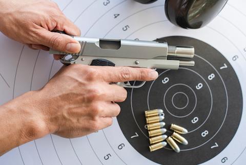 A person loading a gun over a grey and white bulls eye target