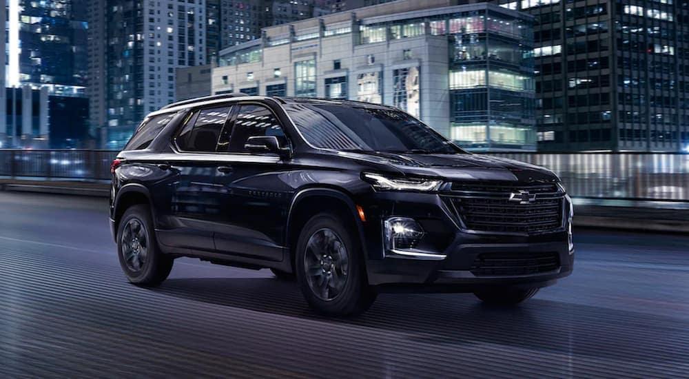 A black 2023 Chevy Traverse Midnight Edition driving on a city street at night.