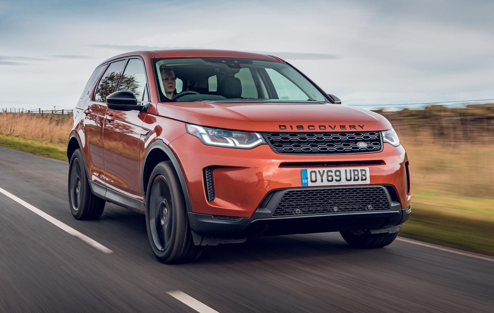 an orange land rover discovery sport driving on a road