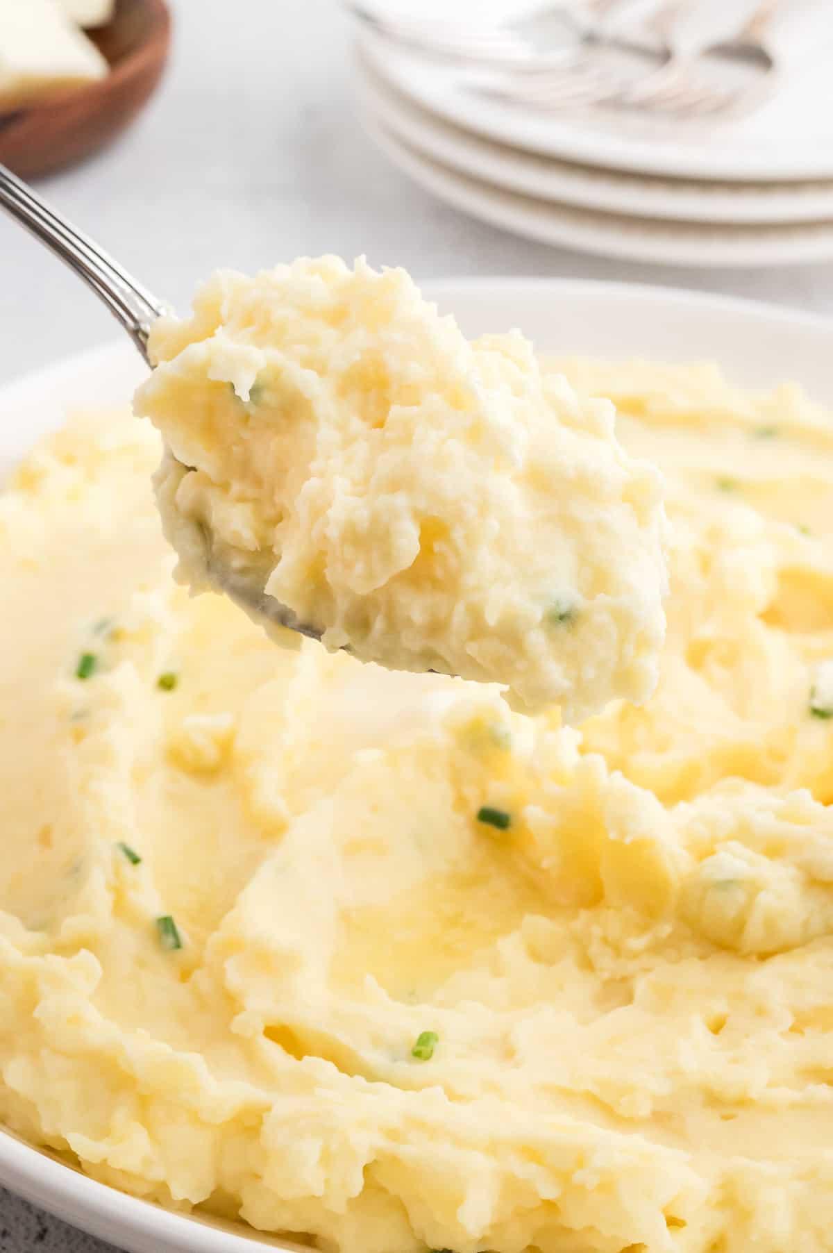 A scoop of mashed potatoes, with a bowl of potatoes in the background.