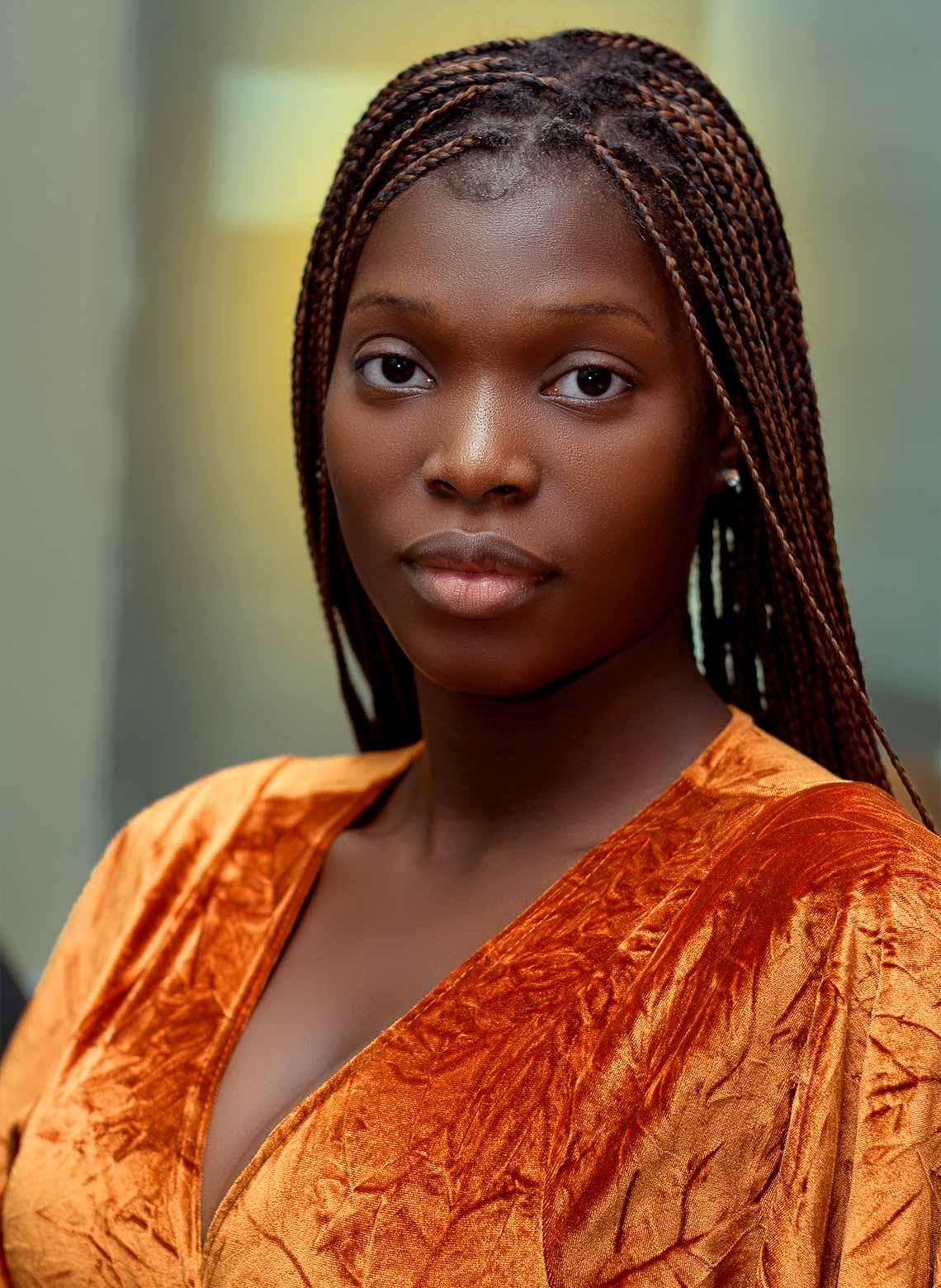 person wearing orange velvet top with long, small knotless braids and looking straight ahead